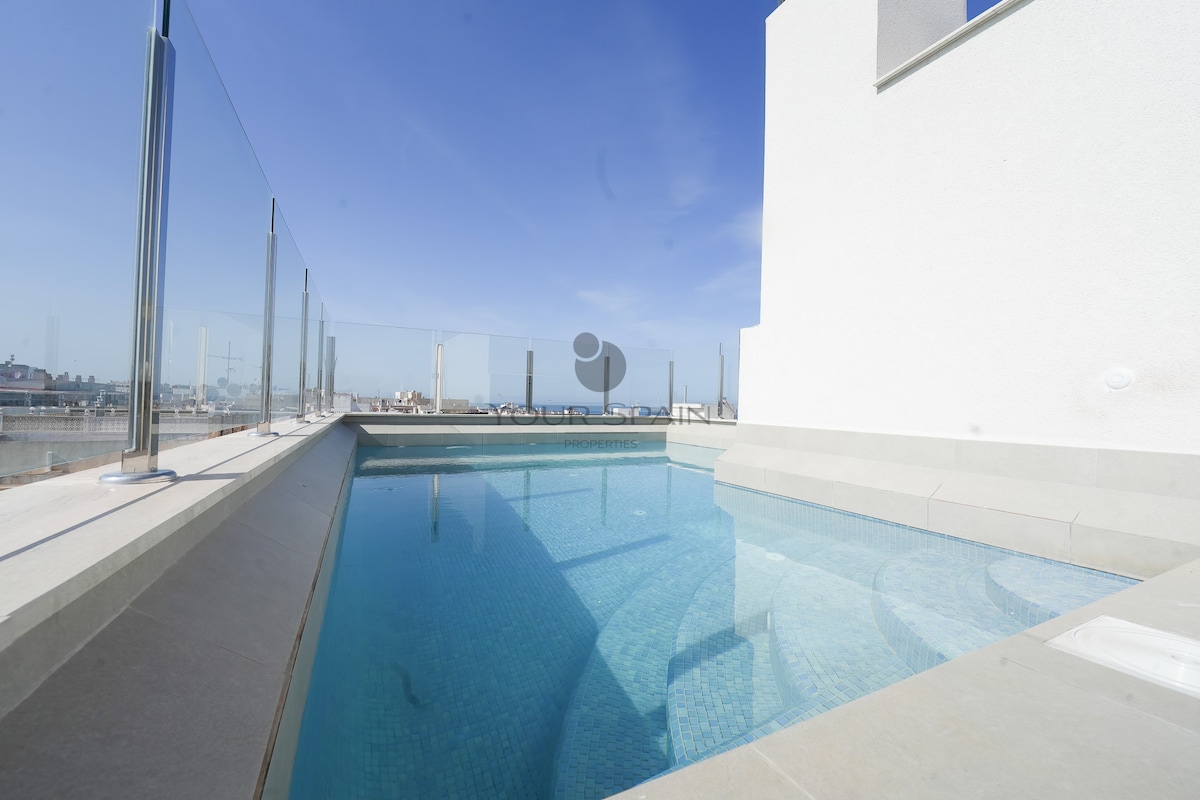 A rooftop pool is surrounded by glass railings, offering unobstructed views of the sky. The water's surface reflects light, enhancing the serene atmosphere. The pool's edges feature smooth stone finishes, seamlessly integrating with the rooftop layout.