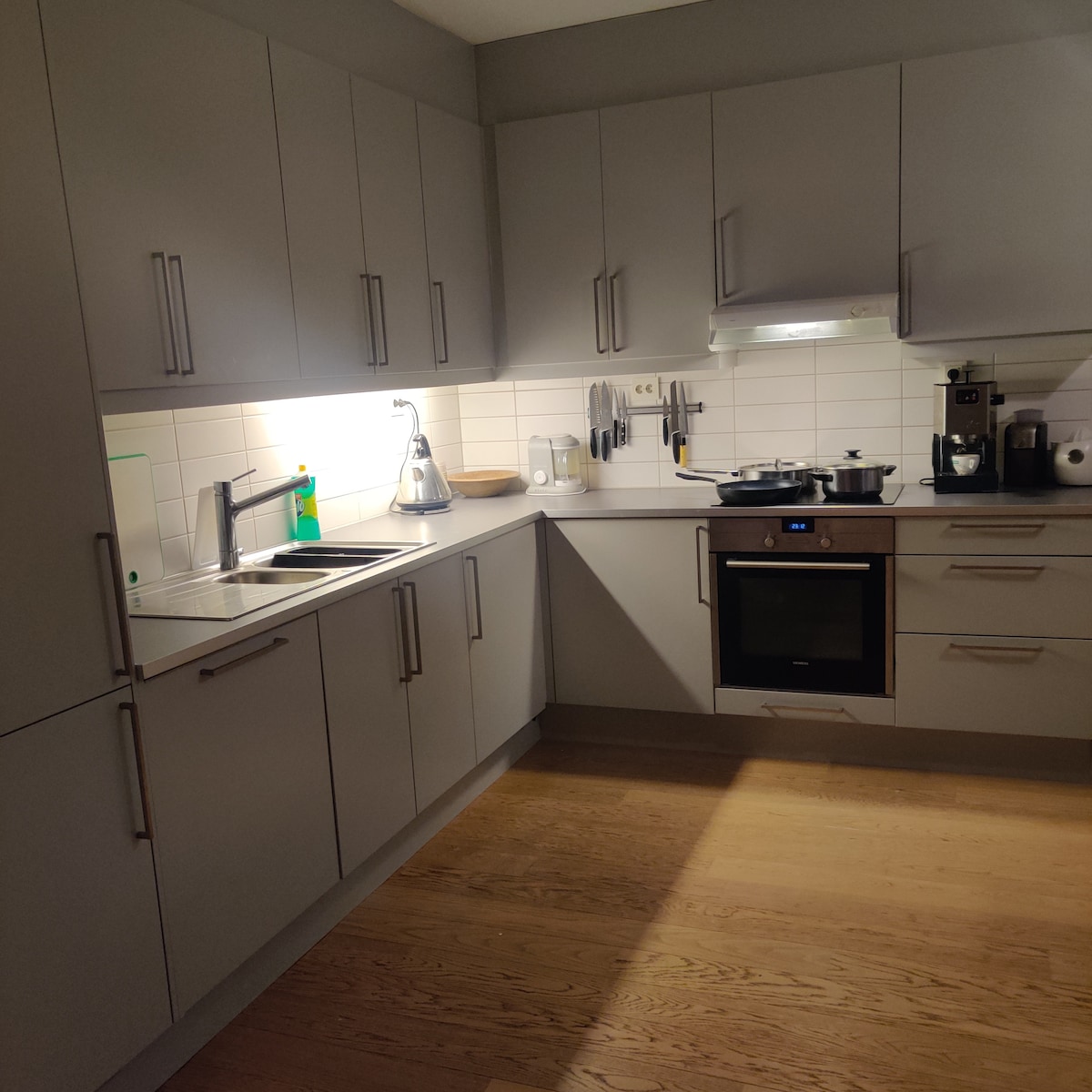 A modern kitchen features sleek, gray cabinetry with ample storage. Counter space is provided for food preparation, complemented by a stainless steel sink and faucet. Cooking appliances include an oven and stovetop, while a small collection of kitchen tools is organized on the wall.