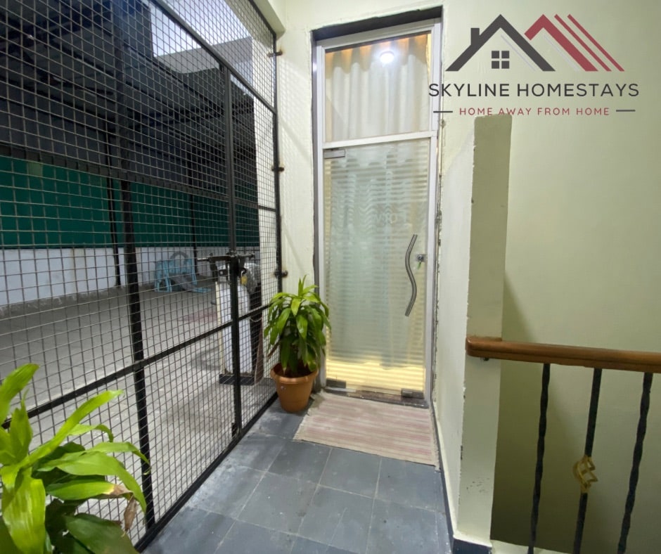 A secured entrance area is featured, highlighted by a glass door flanked by potted plants. The flooring is dark, complementing the indoor and outdoor connectivity through the adjacent wire mesh fencing.