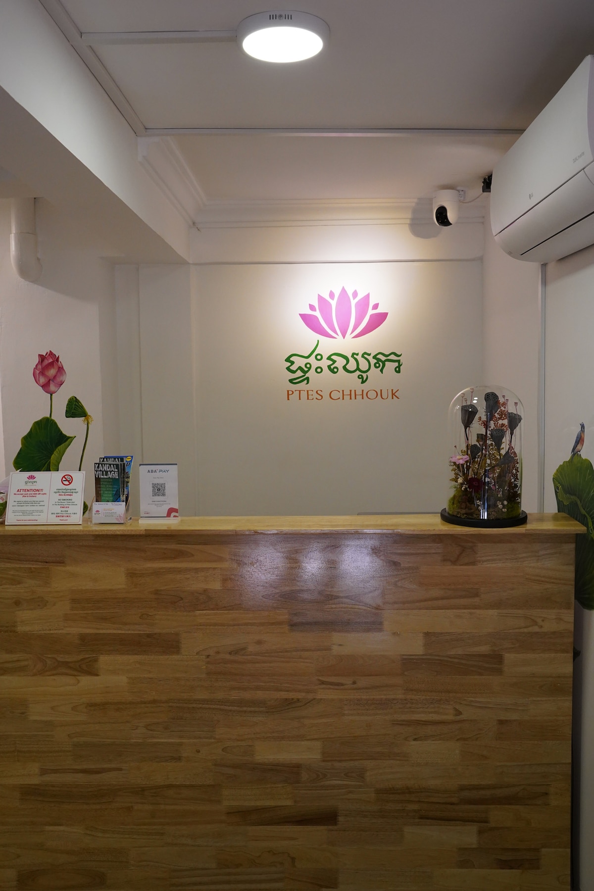 A welcoming reception area is showcased with a wooden counter and a vibrant logo featuring a lotus flower. The space is illuminated with soft lighting, and decorative elements including a glass exhibit with natural accents are visible, complementing the clean and tidy environment.