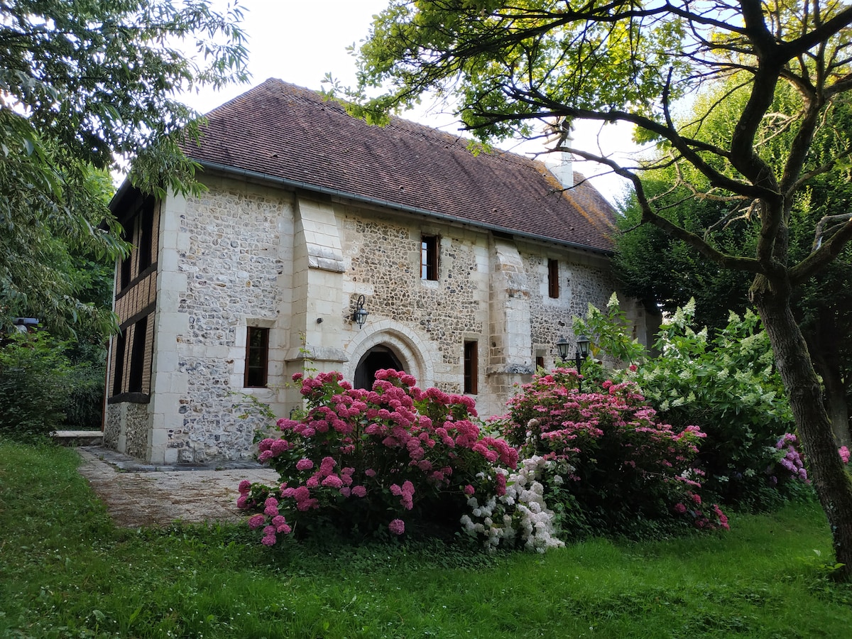 The exterior of the historic chapel is highlighted by a blend of stone and timber, surrounded by a lush garden. Colorful hydrangeas bloom near the entrance, contributing to the natural setting, while mature trees provide shade to enhance the serene outdoor environment.