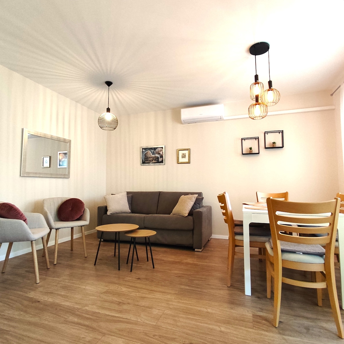 An inviting living and dining area features a comfortable sofa and a small coffee table surrounded by four chairs. A dining table sits nearby, complemented by neutral wall colors and decorative accents. Soft lighting is provided by modern pendant lights, creating a cozy ambiance.