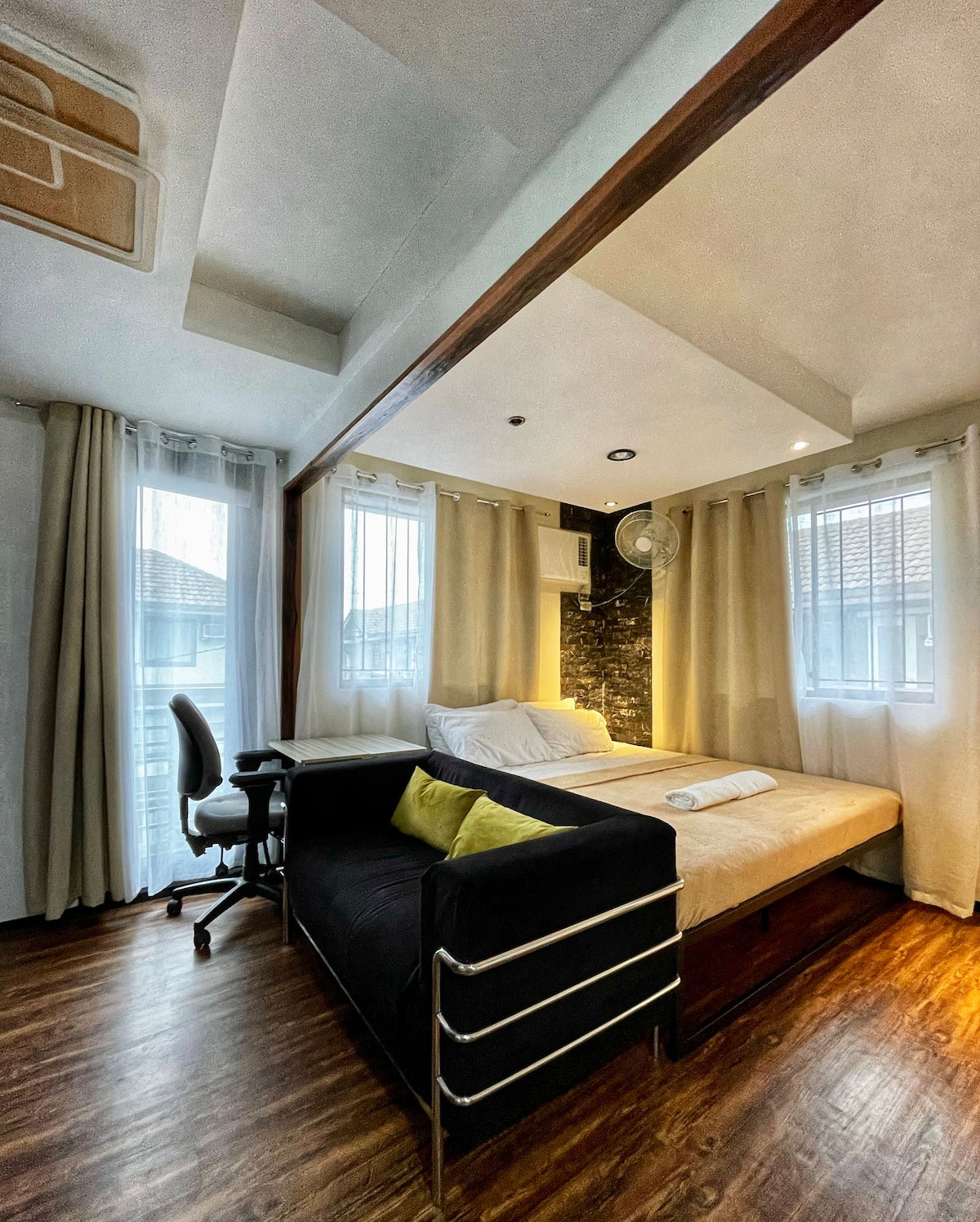 Светло, модерно студио со подигнат кревет, топли дрвени подови и прозорци од подот до таванот. Неутралните завеси, удобниот кауч и бирото создаваат удобен, добро осветлен простор.