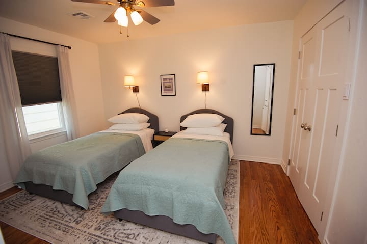 ห้องนอนกลางมีเตียงเดี่ยว 2 เตียง โต๊ะข้างเตียงแบบใช้ร่วมกันพร้อมพาวเวอร์แบงค์หลายพอร์ต มีชั้นวางกระเป๋าเดินทาง 2 ชั้นในตู้เสื้อผ้า