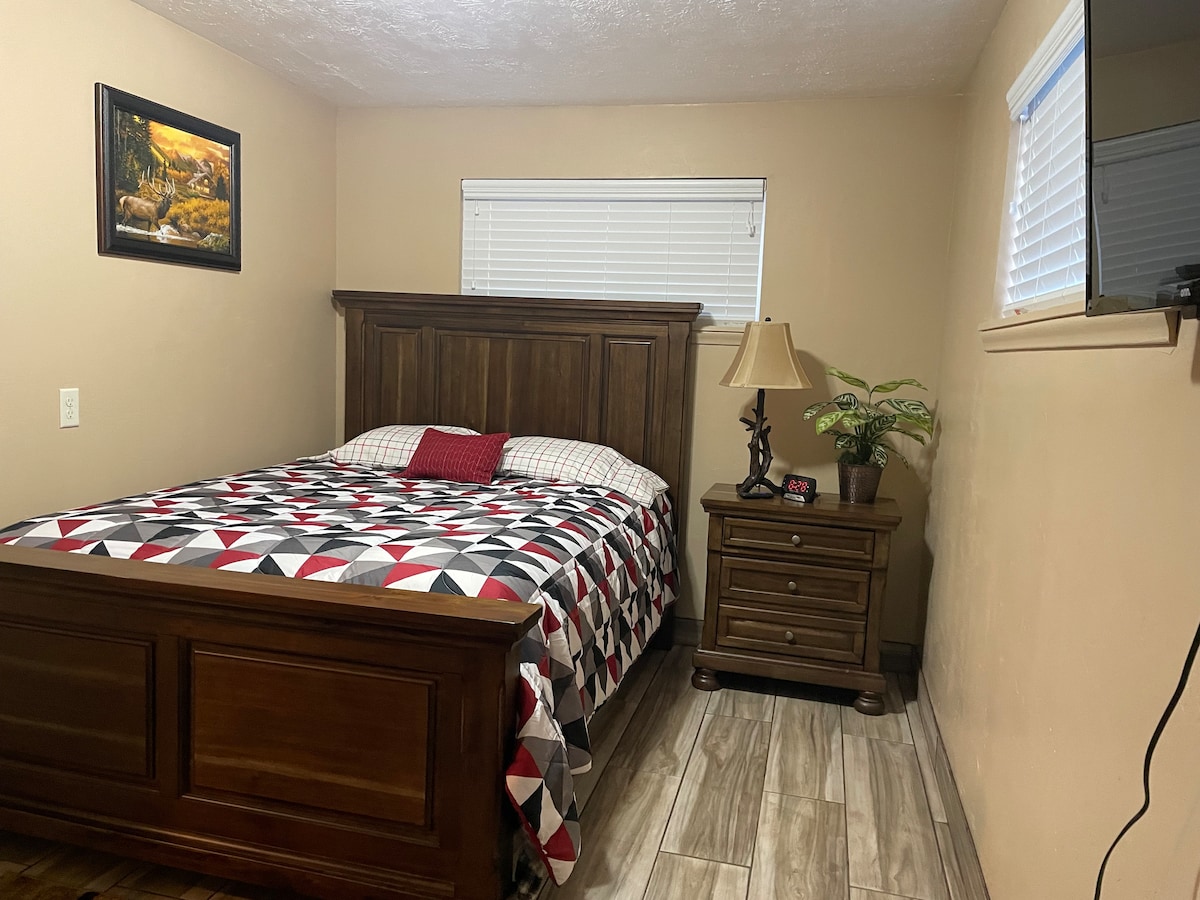 Se muestra una cama tamaño queen con una mesa de noche, un reloj inteligente y un televisor, y es más grande de lo que aparece en la imagen. Esta habitación también cuenta con un armario para que cuelgues tu ropa. 