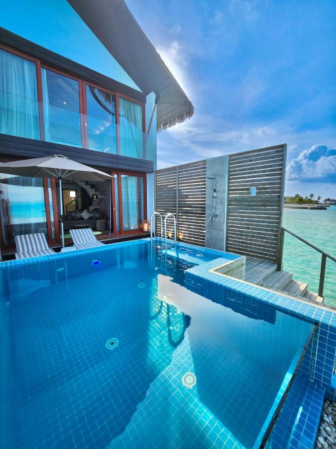 A private plunge pool is situated outside the duplex villa, featuring clear blue water and a small set of stairs leading to it. Two lounge chairs are placed beside the pool on a spacious sun deck, with glass doors of the villa visible in the background.