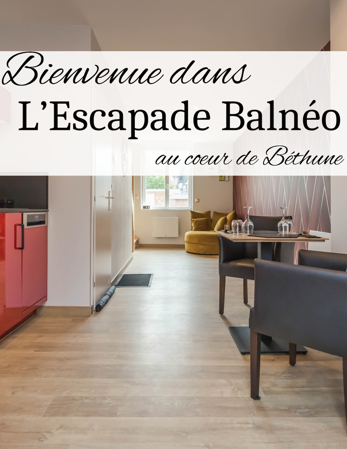 An inviting entrance is showcased, featuring a cozy seating area and a modern kitchenette with red cabinetry. A table for two is set, inviting relaxation. Natural light fills the space through the window, enhancing the warm tones of the decor.