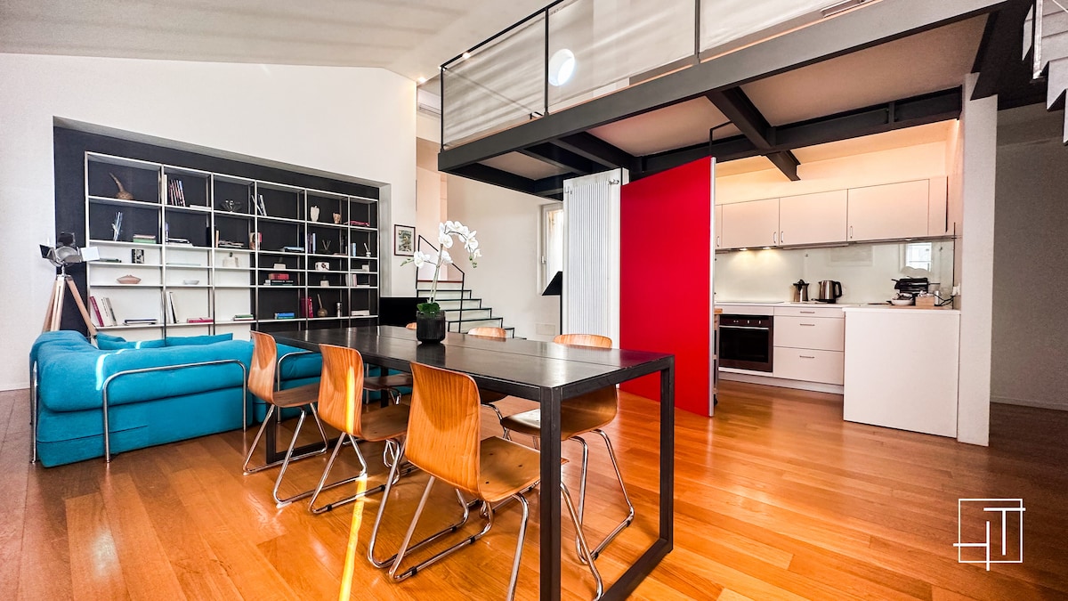 An open-plan living space is featured, showcasing a modern kitchen with sleek cabinetry and a dining area with a dark table surrounded by wooden chairs. A blue sofa adds a pop of color, while large windows fill the area with natural light.