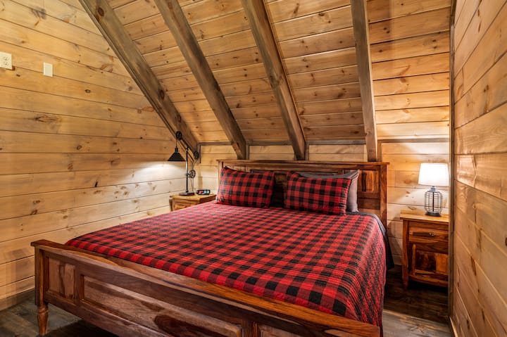 חדר השינה בלופט מציע מיטת קינג עם מזרן עם קצף זיכרון מוקף בשולחנות ליד המיטה עם מנורות, כולל ארון ומתלה מזוודות לאחסון.