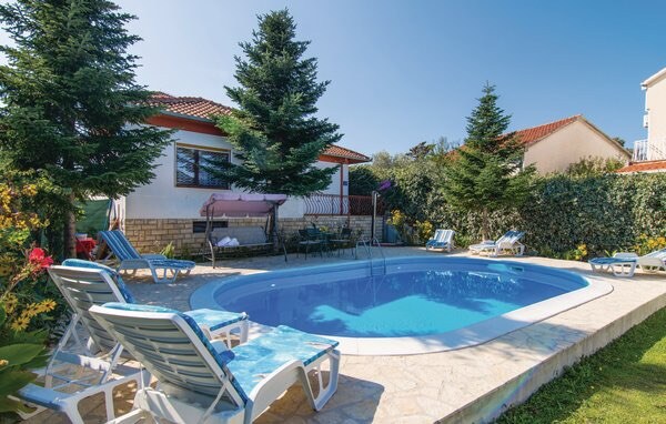 A private outdoor pool is surrounded by lounge chairs, providing a relaxing space for sunbathing. Tall greenery lines the perimeter, enhancing privacy. A shaded area is available, offering respite from the sun. The villa's exterior is visible in the background, contributing to a serene environment.