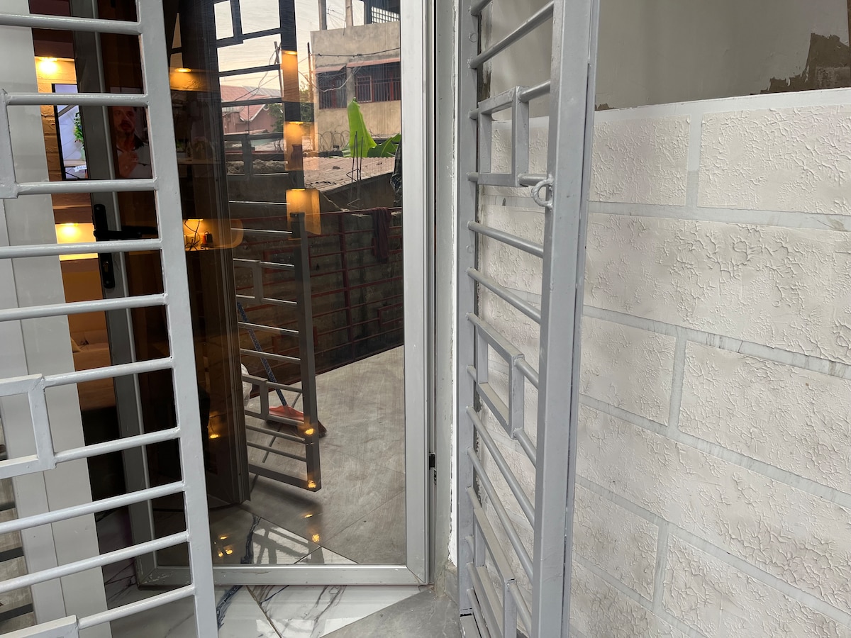 A modern entrance features sleek metal grilles beside a large glass door. Reflections of light can be seen on the glass and the surrounding walls, creating a sense of openness while maintaining security.