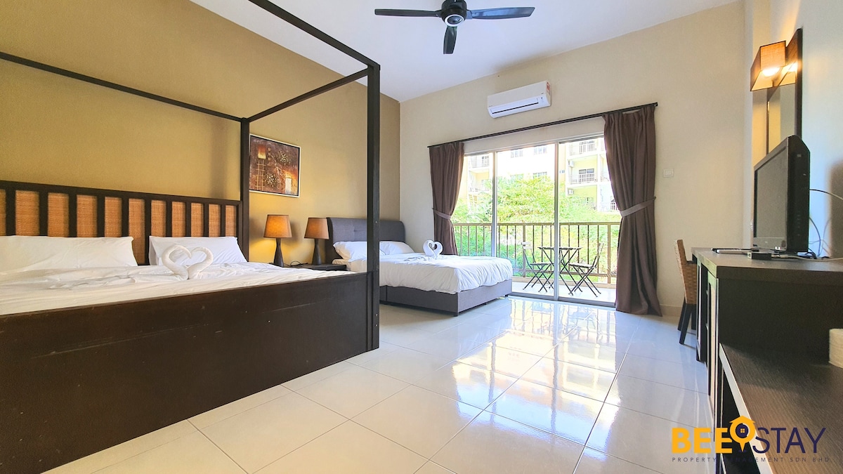 A spacious studio features two queen beds, each with decorative pillows. A balcony is visible, providing natural light and a view of the outdoor area. A ceiling fan and a dresser are included, enhancing the functionality of the space.