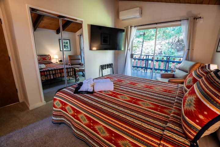Bedroom opens up to exterior rear deck with views of the forest, large flat screen tv, AC unit, and closet. This bedroom is on the 3rd level of the cabin. 