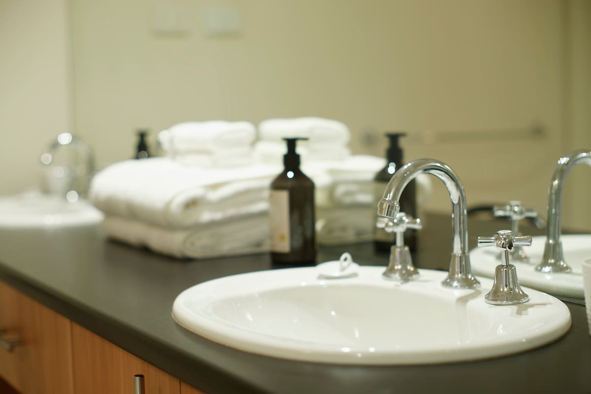 A modern bathroom sink sits beside neatly stacked fluffy towels and a variety of complimentary toiletries in dark glass bottles. The sleek countertop provides a functional space, with a polished faucet adding an elegant touch to the clean and inviting environment.