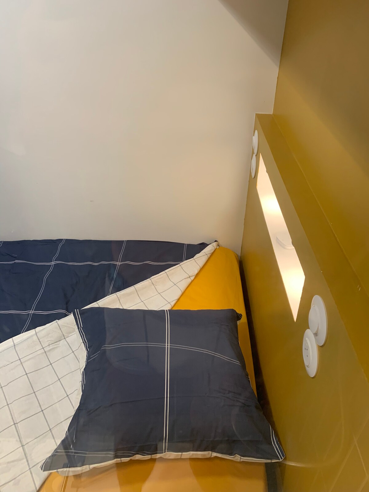 Kichwa cha kitanda kilicho na plagi na sehemu ndogo ya simu yake ya mkononi. 