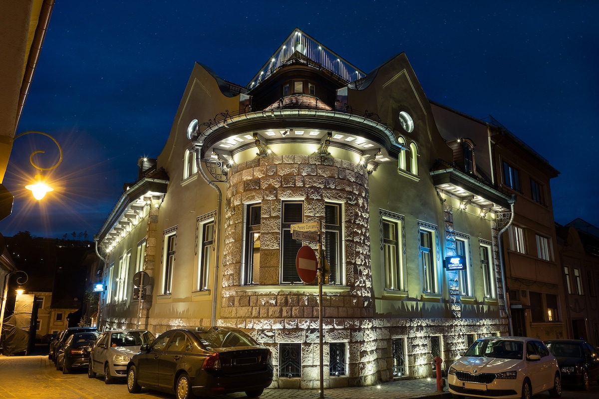 The exterior of the property showcases an architecturally distinctive building illuminated at night, highlighting its stone facade and decorative features. Soft lighting enhances the structure's unique shape, while parked cars line the street in front, contributing to the urban atmosphere.