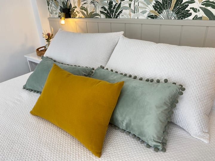 Descansa en una cama diseñada para tu confort, con suaves cojines en tonos cálidos que invitan al relax. El cabecero y el papel pintado con motivos florales crean un ambiente fresco y acogedor. ¡Haz de tu estancia una experiencia reconfortante!