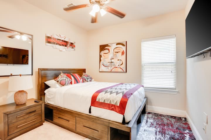 Dormitorio cálido y acogedor con una cama cómoda, decoración elegante, luz natural y un televisor montado en la pared para relajarse al final del día.