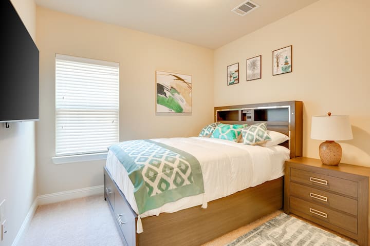 Cómodo dormitorio con tonos suaves, una acogedora cama, almacenamiento junto a la cama y un televisor montado, perfecto para relajarse y recargar energías.