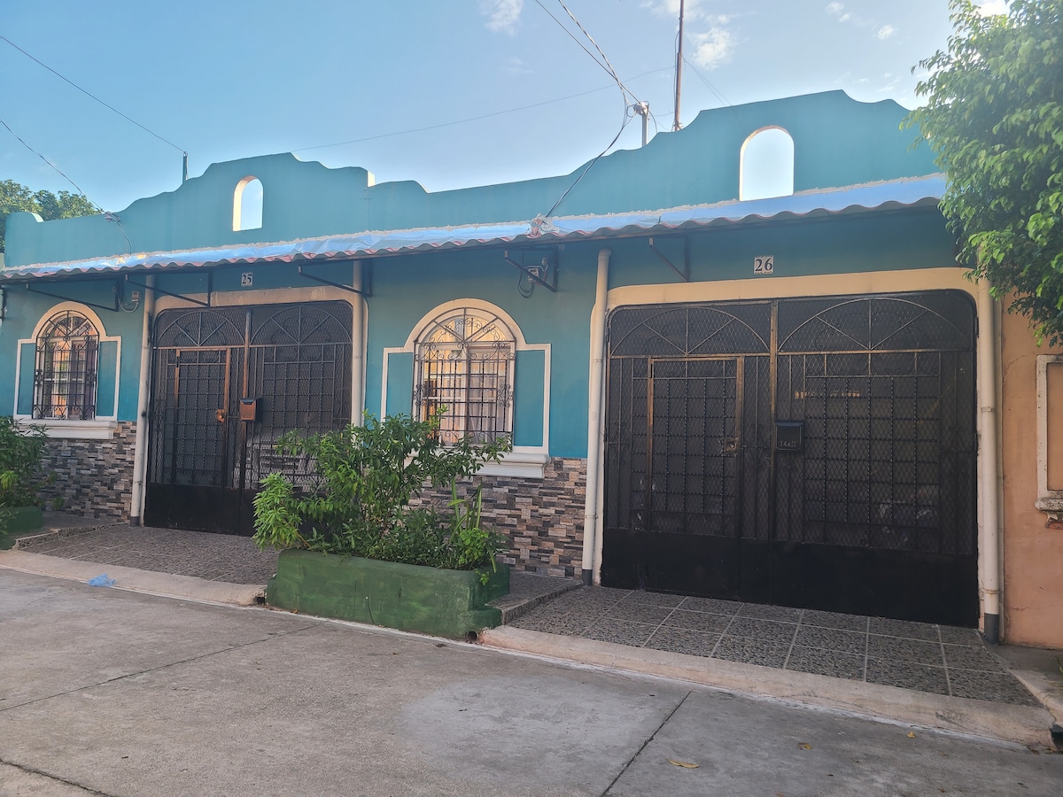 The exterior of a building is captured, featuring a vibrant blue facade with decorative architectural details. Two separate entrances are visible, framed by black wrought iron gates. Green planters line the sidewalk, adding touches of greenery to the welcoming environment.