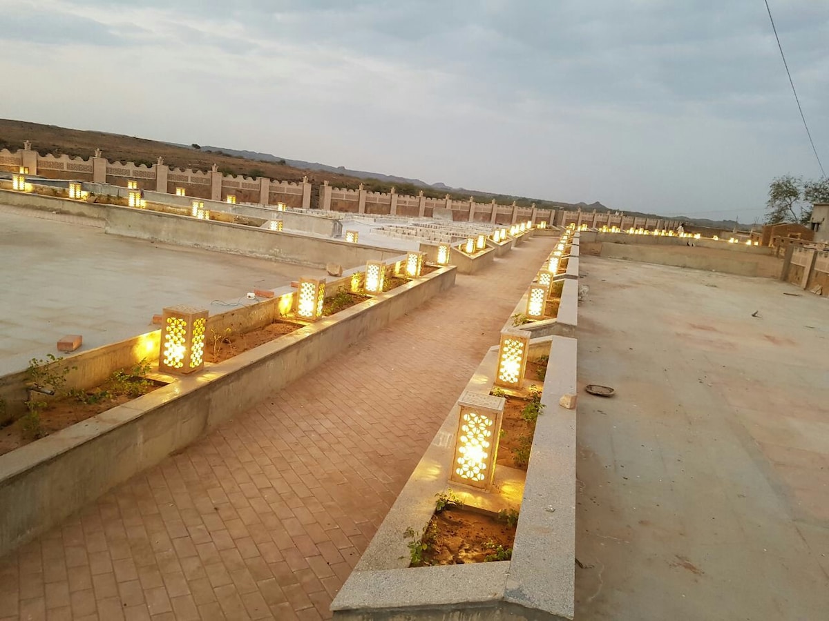 A landscaped outdoor area is featured with stone pathways lined by decorative lighting. Low planters with greenery are interspersed along the path, creating a serene environment. The sky is overcast, contributing to a peaceful ambiance in the expansive space.