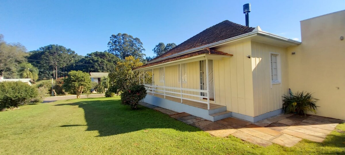 The exterior of a charming house is shown, featuring a covered porch and light-colored siding. A well-maintained lawn surrounds the property, with shrubbery and trees providing a natural backdrop. The area is sunny, under a clear blue sky.