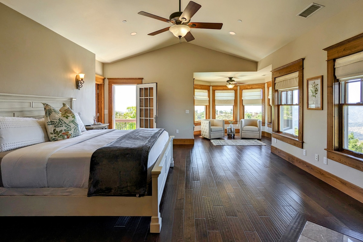 Main house primary suite with king bed, full bathroom, sitting area, flat screen TV, walk-in closet, and balcony