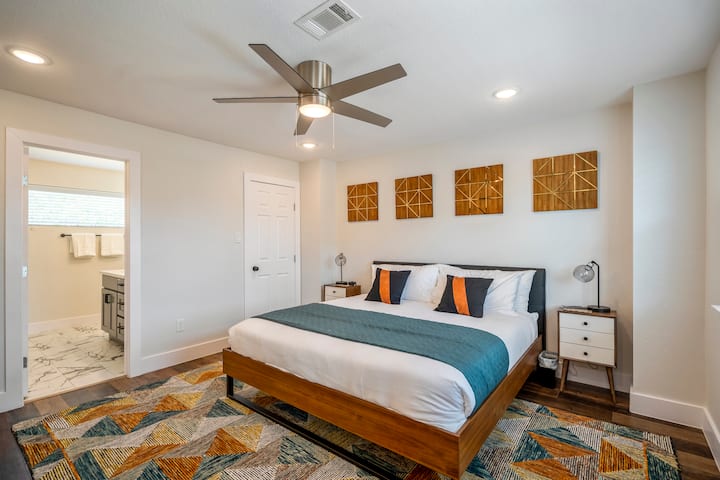 Upstairs Bedroom with King Bed with a modern geo design that contains a personal television, desk with chair, walk-in closet, and private 2 sink ensuite bathroom with standup shower. 
