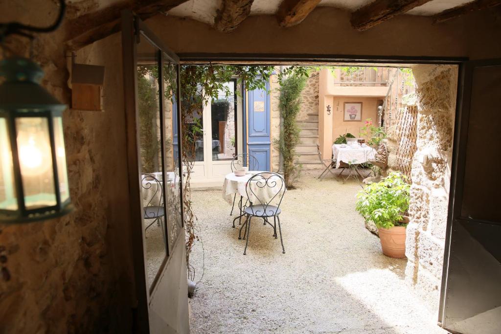 A serene courtyard is framed by rustic stone walls, with two bistro tables set for dining. Lush greenery provides a natural backdrop, while a bright blue door adds a pop of color. Soft light filters through, creating a welcoming ambiance.