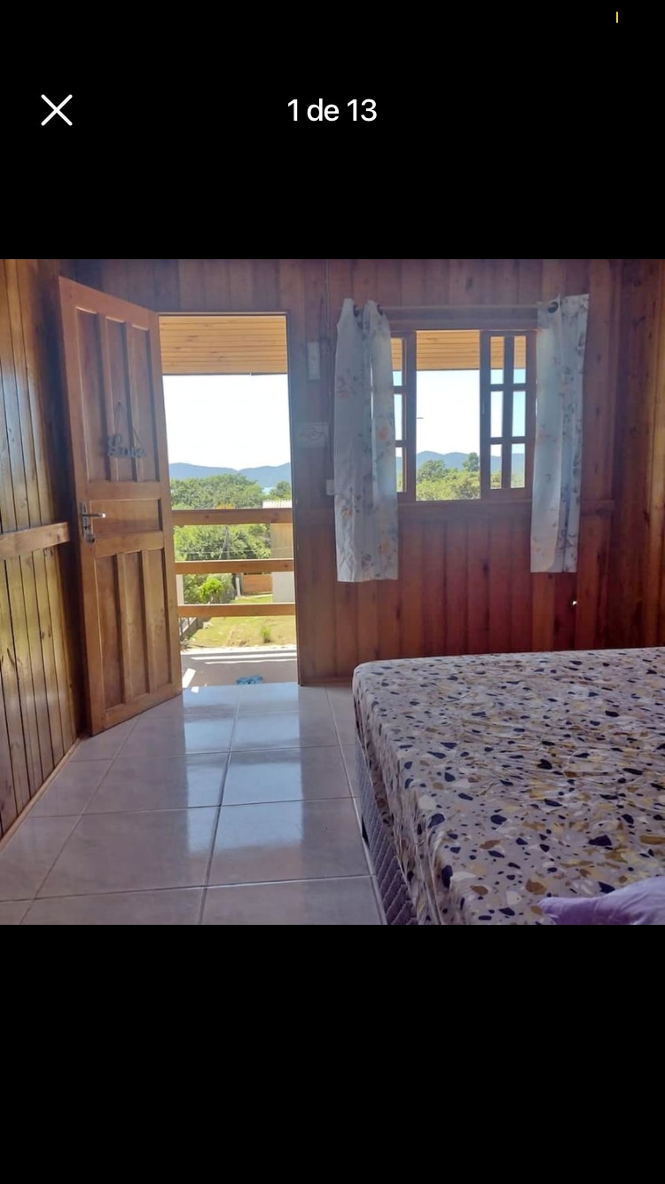 A wooden room features an inviting spacious bed with a patterned bedspread. Large open doors allow for natural light and a view of the surrounding landscape. Light-colored curtains frame the windows, enhancing the connection with the outdoors.