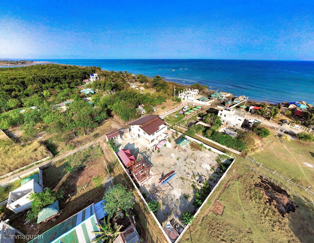 An aerial view showcases the property surrounded by greenery and a serene coastline. The layout reveals a spacious outdoor area, with hints of structures and paths leading towards the sea, illustrating the peaceful and private setting near the water.