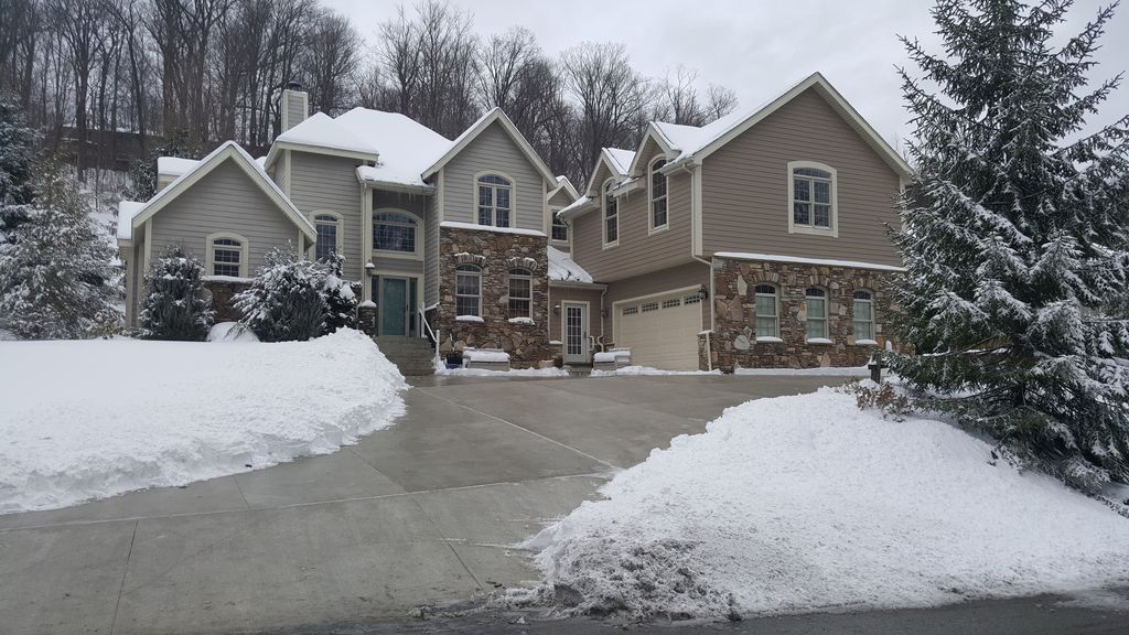 A spacious single-family home is showcased, set against a backdrop of snow-covered ground and trees. The exterior features a blend of stone and siding, with a large driveway providing ample parking space. The snowy landscape enhances the home's charm.