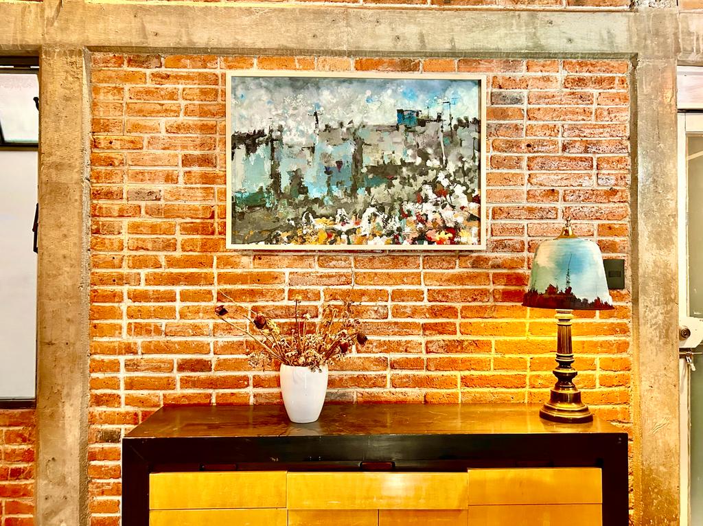 An artistic space is highlighted by a vibrant painting hanging on a brick wall, complemented by a table lamp with a colorful shade. A wooden console table stands beneath, featuring a decorative vase filled with dried flowers, creating a warm and creative atmosphere.