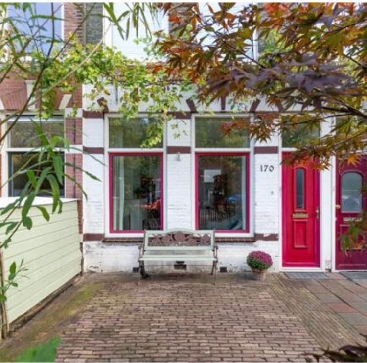 The exterior of the property features a brick path leading to two vibrant red doors. A wooden bench is positioned near the entrance, flanked by greenery. Windows in front are framed in white, allowing natural light to illuminate the space behind.