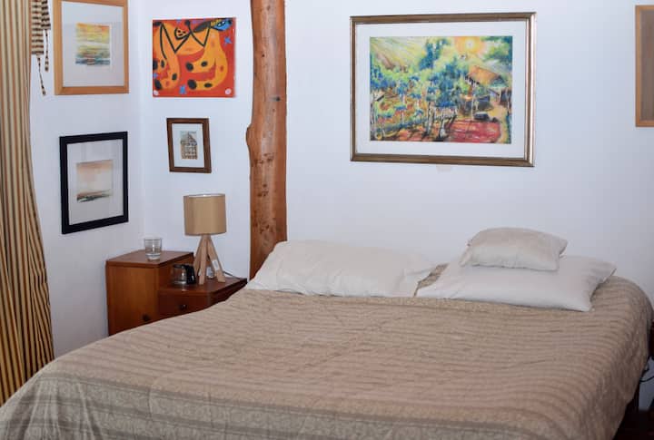 Secondary room, rustic and harmonious. It has a double bed, bedding, wooden bedside tables, and a sample of local artists. 