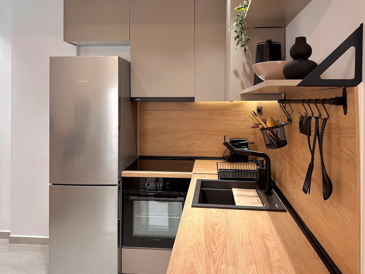 A modern kitchen features sleek cabinetry and stainless steel appliances, including a large refrigerator and oven. Warm wooden countertops provide ample workspace, complemented by a minimalist sink and essential kitchen utensils neatly organized on a wall-mounted rack.