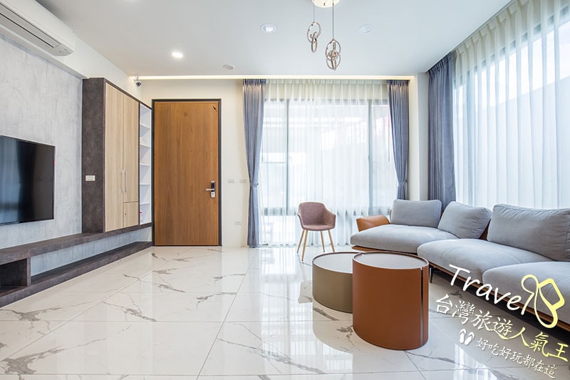A modern living area is showcased with natural light filtering through sheer curtains. A soft gray sectional sofa offers ample seating next to a round coffee table. A stylish chair adds to the minimalist aesthetic, while a wall-mounted television completes the space.