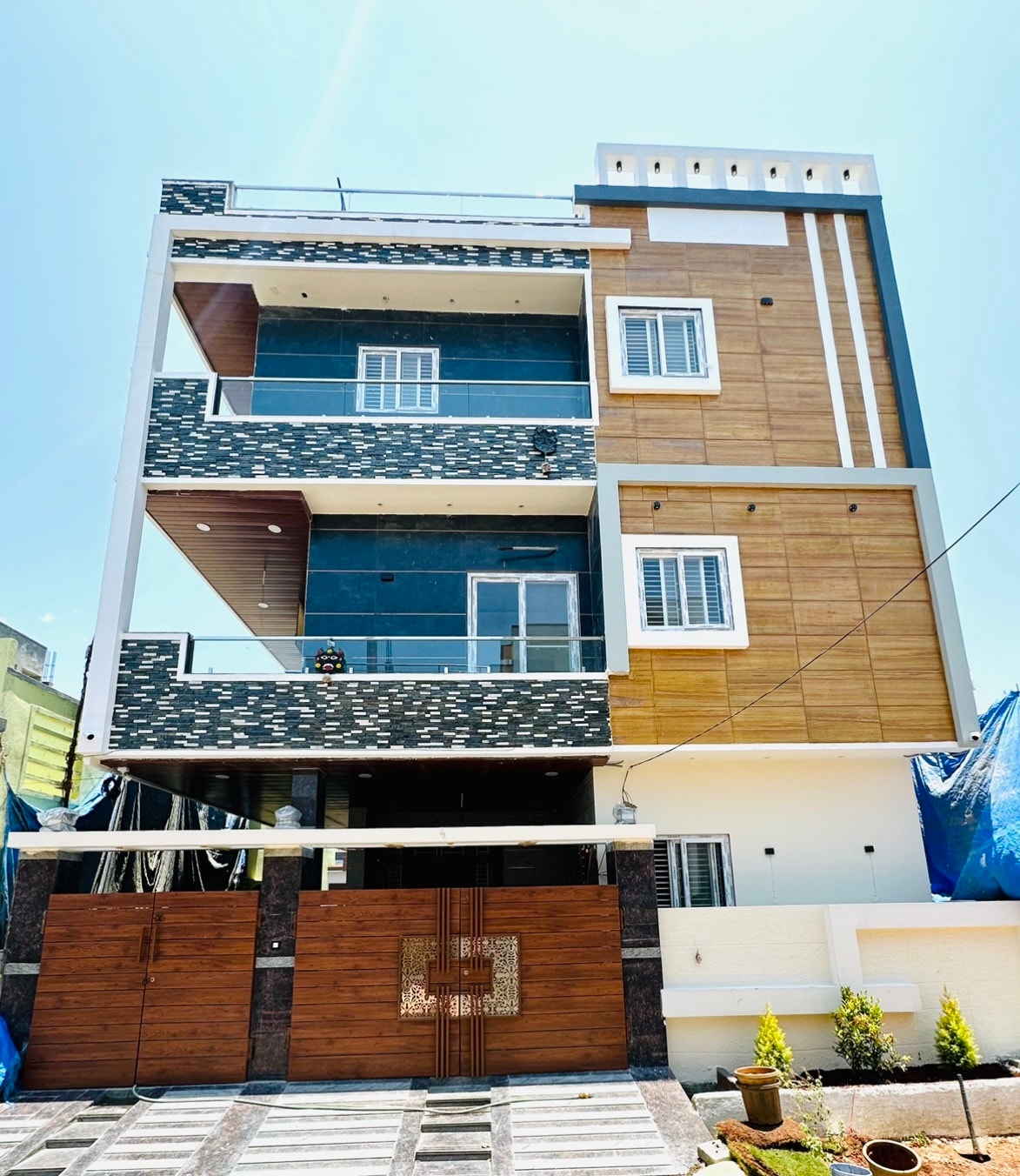 The exterior of a three-story building is showcased, featuring a combination of modern paneling in wood and dark tones. A stylish gate made of wood is visible, providing access to the property. The facade includes multiple windows designed for natural light.