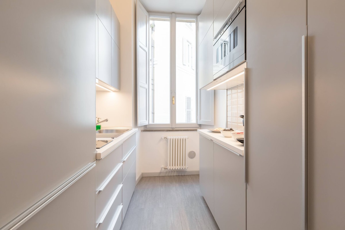 The kitchen features a modern design with sleek cabinetry and integrated appliances. A large window allows ample natural light, enhancing the space. Cooking essentials and utensils are provided, and there is a comfortable arrangement for meal preparation.
