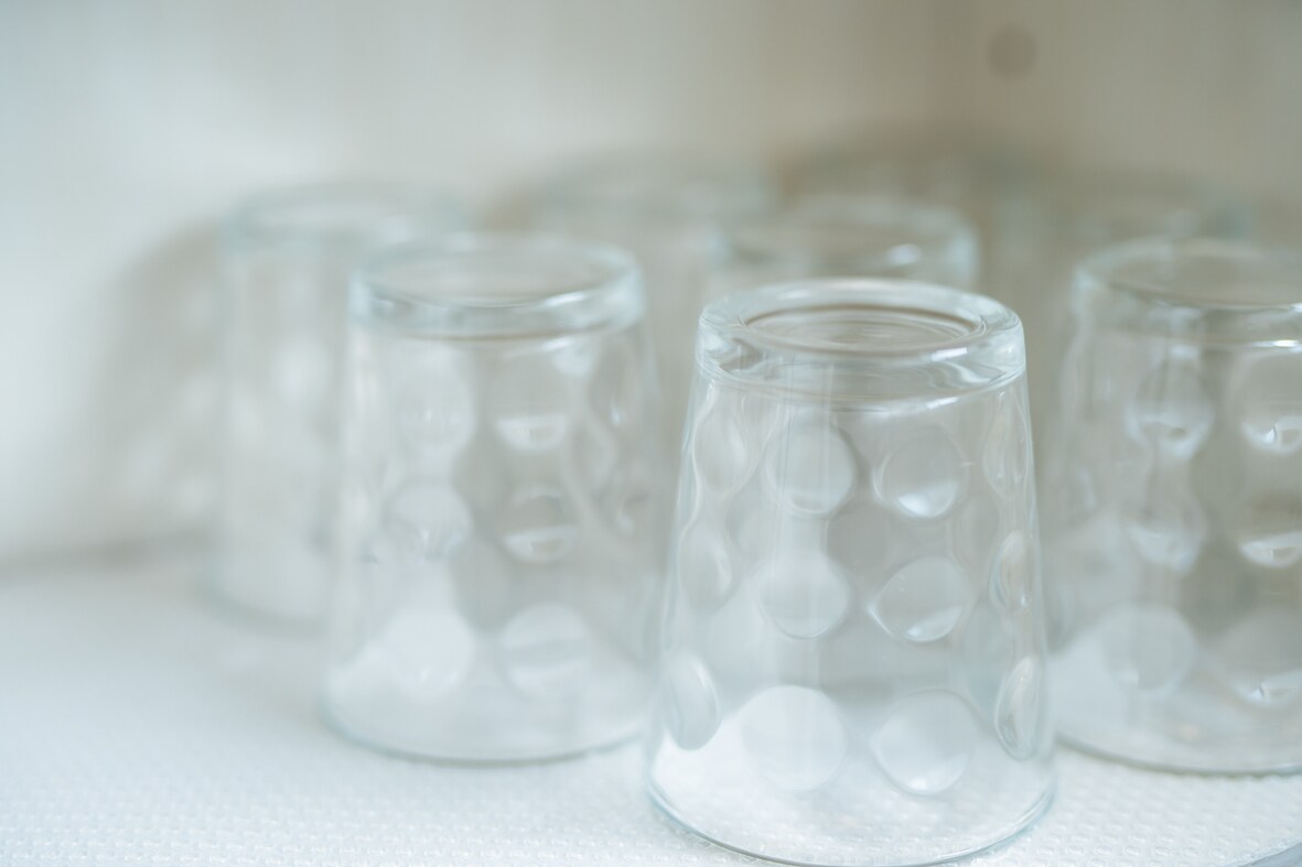 Several clear glass cups are arranged on a light surface, featuring an embossed bubble pattern. The glasses vary slightly in orientation, creating an appealing visual arrangement. Their simple design allows for easy integration into any dining or kitchen setting.