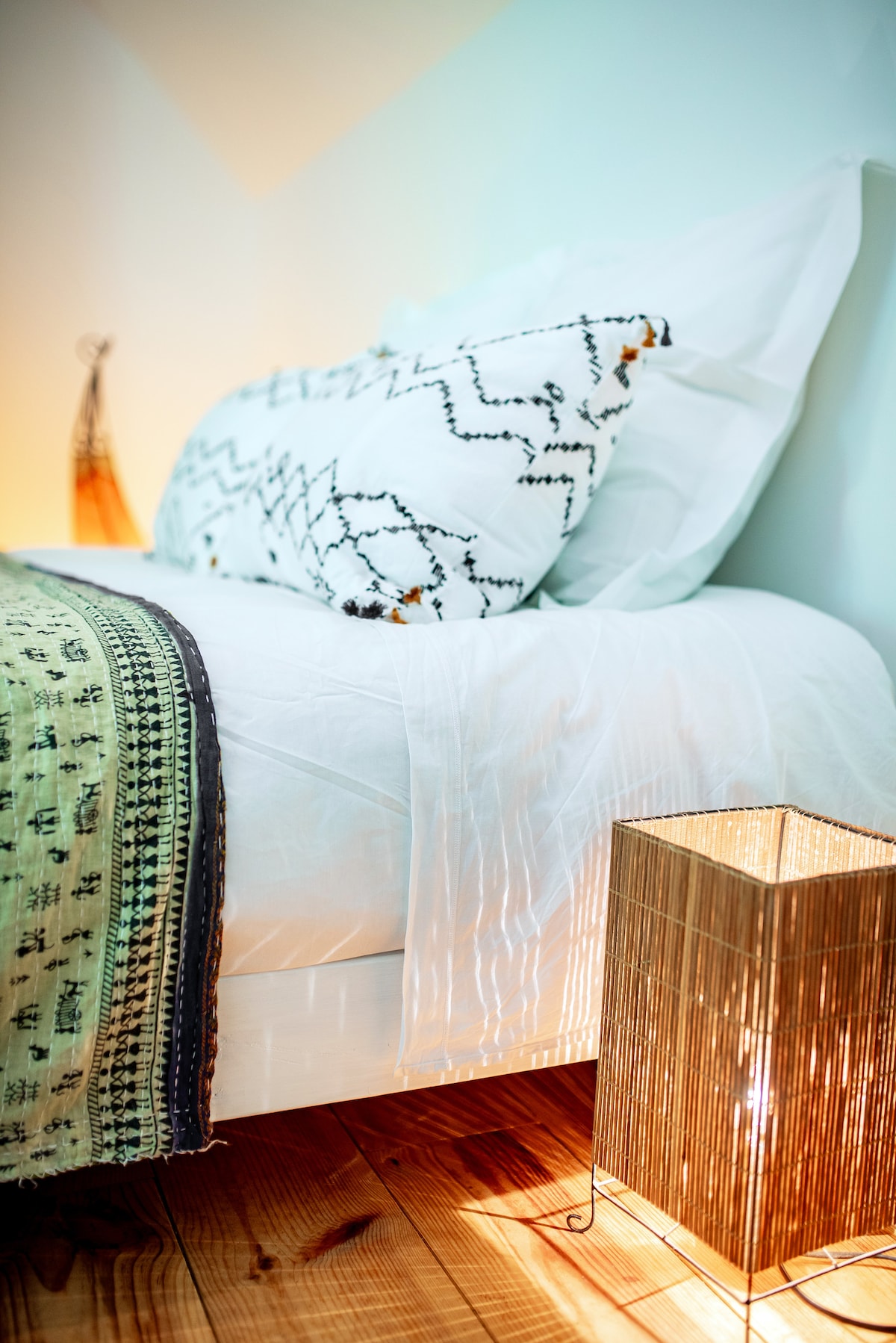 A cozy corner of the bedroom features a spacious bed adorned with decorative pillows and an elegant blanket. A soft light emanates from a stylish bedside lamp, illuminating the warm wooden floor.