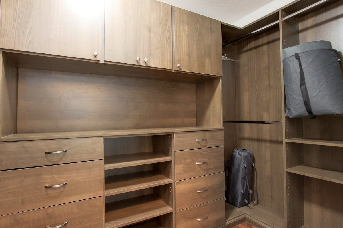 A spacious walk-in closet features a combination of built-in shelves and drawers. The wooden cabinetry offers a modern finish, with ample storage space available for clothing and personal items. A hanging rod is positioned on the left side for additional garment storage.