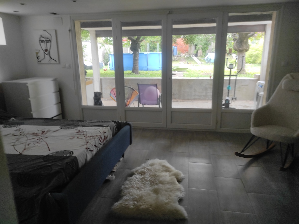 A spacious room features a double bed with decorative bedding positioned near large glass doors. A private terrace and shared garden are visible through the doors, complemented by outdoor seating. A cozy area rug adds warmth to the tiled floor.