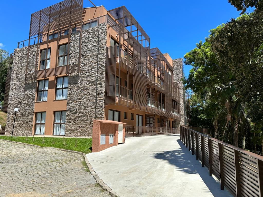 A modern multi-story building showcases a blend of stone and sleek materials. Large windows allow natural light to fill the interior, while an inviting pathway leads to the entrance. Lush greenery surrounds the property, enhancing a sense of connection to nature.