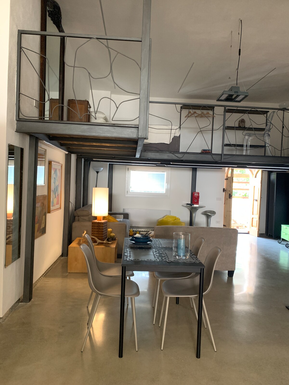 An open living area features a dining table set for four, complemented by modern white chairs. A cozy seating arrangement is visible across the room, while a loft structure provides additional space. Soft lighting and a touch of artwork add to the tranquil ambiance.