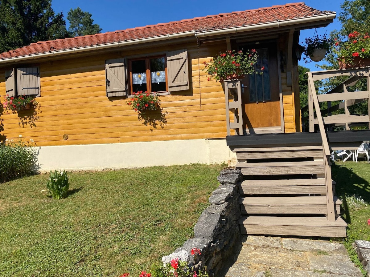 A charming wooden chalet features a welcoming entrance with a sturdy staircase leading up to the door. Flower boxes hang below the windows, adding a touch of color to the rustic façade. Lush greenery surrounds the property, enhancing its natural setting.