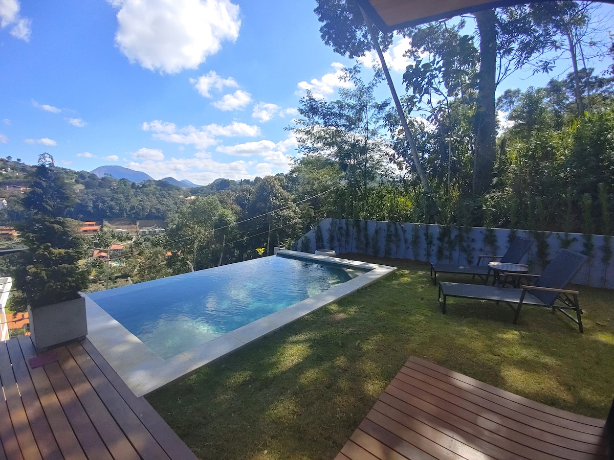 A private infinity pool is surrounded by a lush green lawn, providing a serene view of the valley and distant mountains. Two lounge chairs are positioned beside the pool, inviting relaxation in a tranquil outdoor setting under a sunny sky.
