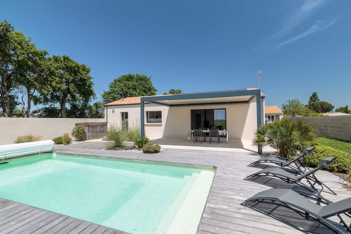 A modern home is depicted against clear blue skies, featuring a serene pool bordered by a wooden deck. Several lounge chairs are arranged nearby on the deck, while inviting greenery provides a backdrop that enhances the outdoor setting.