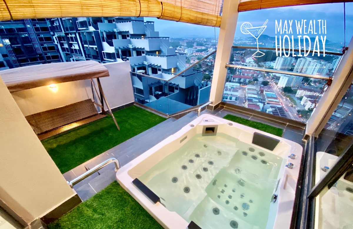 A private jacuzzi pool is situated on a balcony with a grass-like surface, providing a view of the surrounding city. The jacuzzi features a massage bubble system and is complemented by an adjacent wooden seating area, offering relaxation in an urban setting.