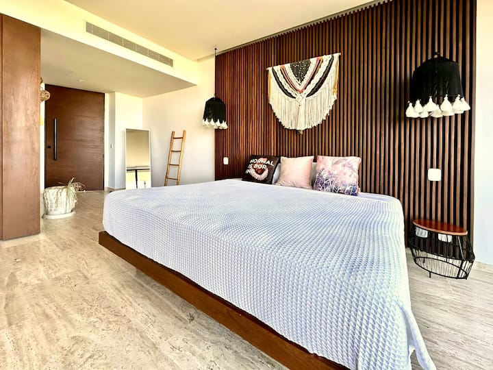 غرفة نوم ثانية بسرير بمقاس كبير ومكتب عمل ومرآة كاملة للجسم وتراس خارجي مع إطلالات جميلة على الغابة